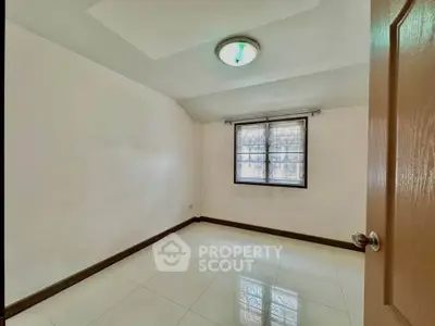 Spacious empty room with tiled flooring and window, ideal for customization.