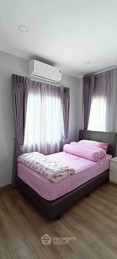 Cozy bedroom with pink bedding, air conditioning, and natural light from two windows.