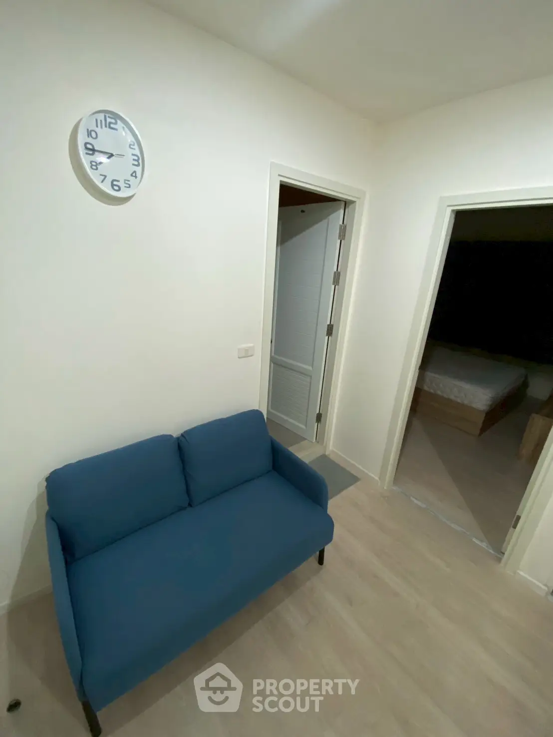 Cozy small living area with blue sofa and wall clock, adjacent to bedroom.