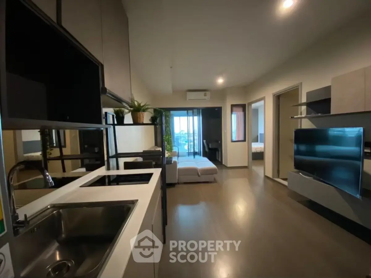 Modern open-layout apartment with sleek kitchen and spacious living area, featuring a large TV and stylish decor.