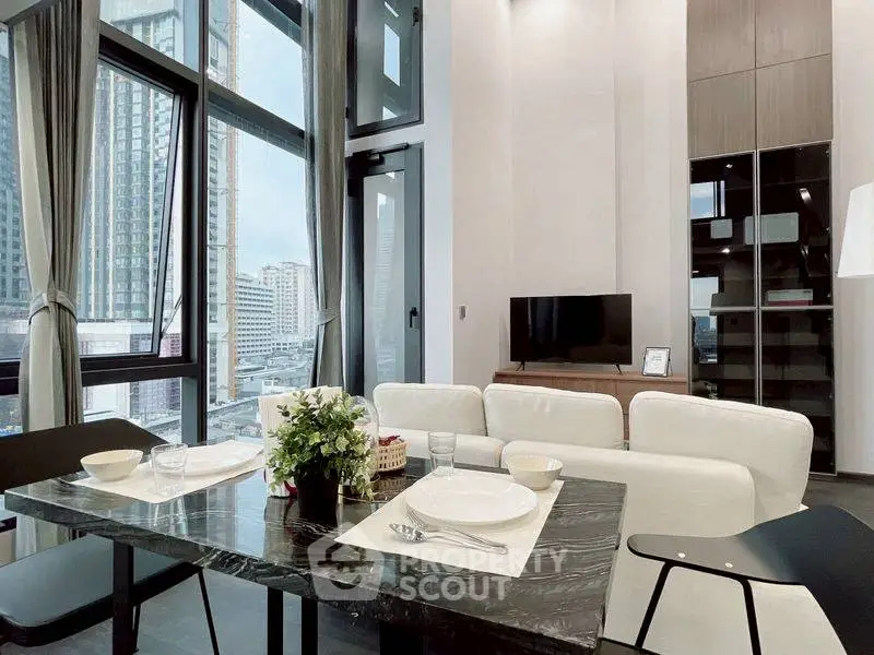 Modern living room with high ceilings and city view, featuring elegant dining setup.