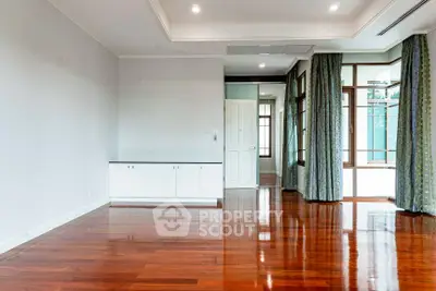Spacious empty living room with polished wooden floors and large windows.