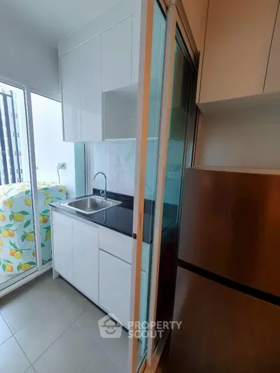 Modern compact kitchen with sleek cabinetry and stainless steel fridge in a bright apartment.