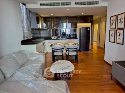 Modern open-layout living room with kitchen, featuring sleek furniture and wooden flooring.