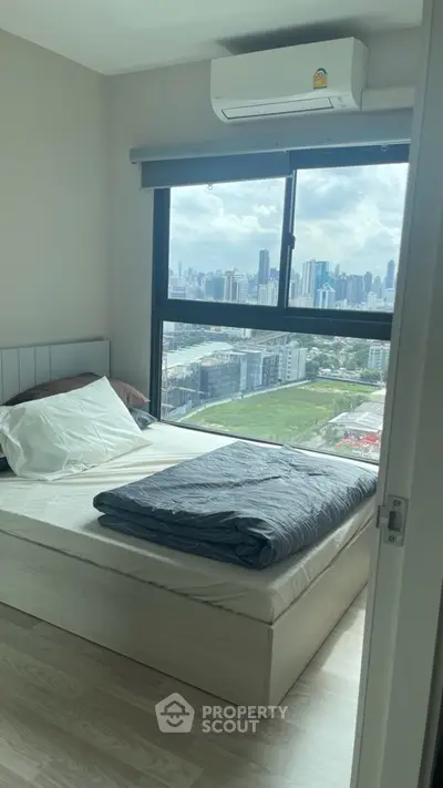 Cozy bedroom with city view, featuring a large window and modern furnishings.