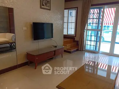 Spacious living room with modern TV setup and elegant decor, featuring large windows for natural light.