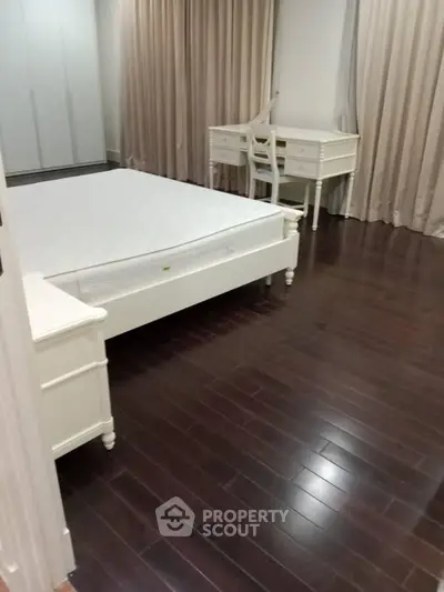 Spacious bedroom with elegant dark wood flooring and classic white furniture.