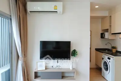 Modern living room with TV, air conditioner, and compact kitchen featuring washing machine.