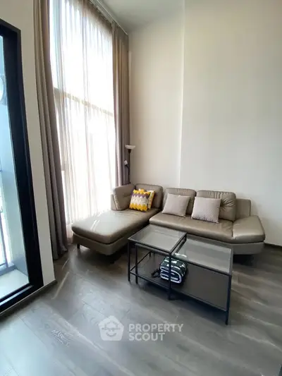 Modern living room with high ceilings and large windows, featuring a stylish sofa and glass coffee table.