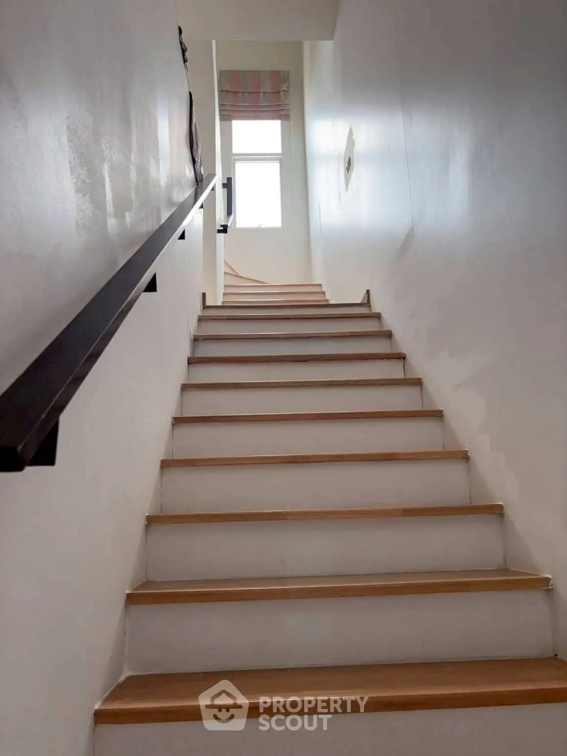 Modern staircase with wooden steps leading to a bright window, showcasing minimalist design.