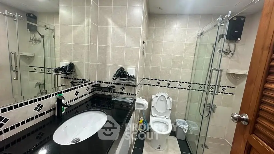Modern bathroom with sleek black countertop and glass shower enclosure.