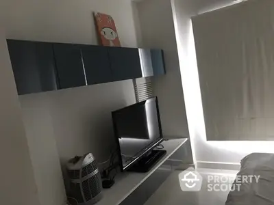 Modern minimalist bedroom with sleek wall-mounted shelves, a flat-screen TV, and ample natural light filtering through a large window.