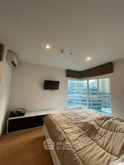 Modern bedroom with city view, featuring a cozy bed, wall-mounted TV, and large windows for natural light.