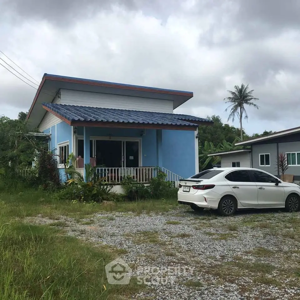 Charming blue house with car parked in front, surrounded by lush greenery and tropical palm trees.
