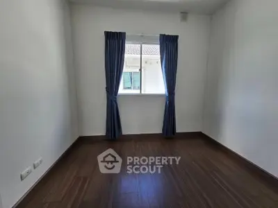 Spacious empty room with wooden flooring and window view, perfect for customization.