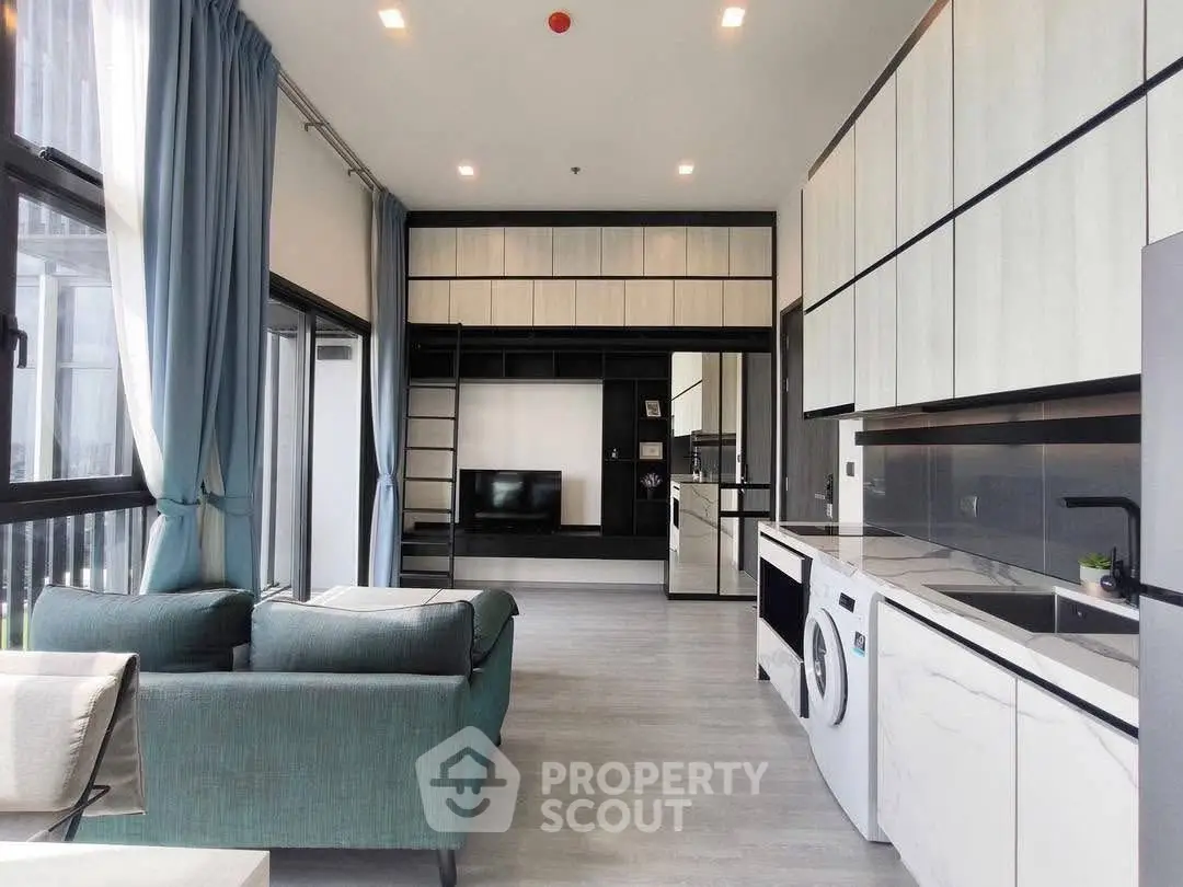 Modern open-plan living room with sleek kitchen and laundry appliances, featuring large windows and stylish decor.