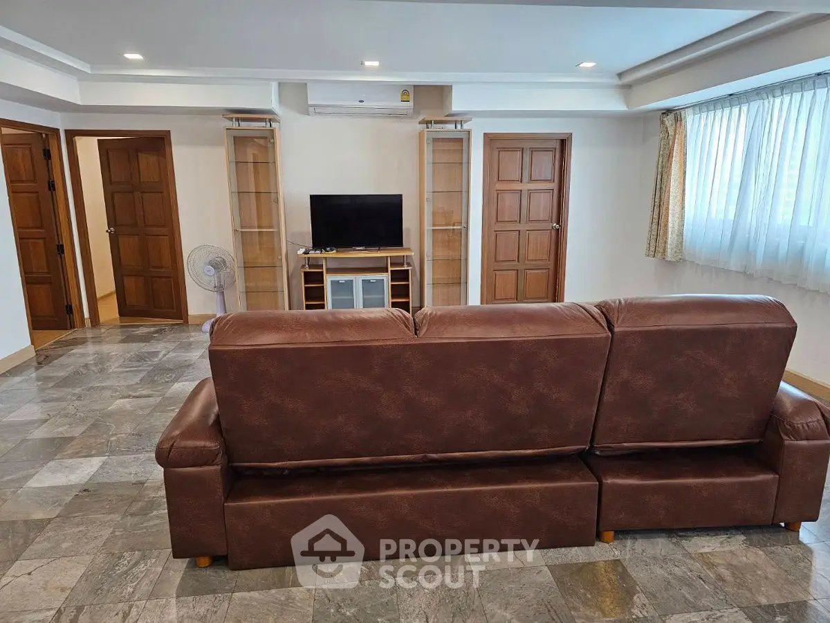 Spacious living room with leather sofa and TV, featuring large windows and elegant flooring.
