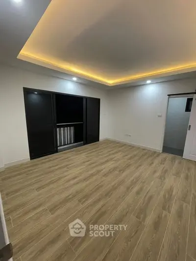 Spacious modern living room with elegant lighting and wooden flooring, featuring a balcony access.