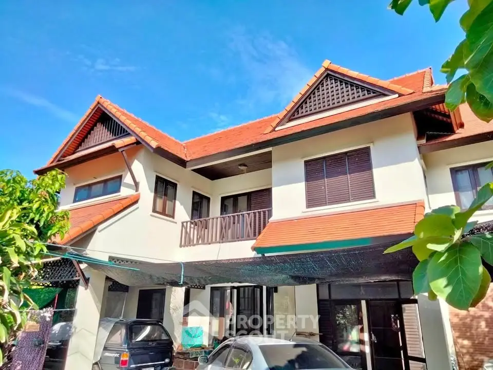 Charming two-story house with red-tiled roof and lush greenery, perfect for family living.