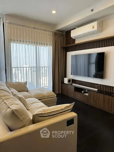 Modern living room with large TV and cozy beige sofa, featuring floor-to-ceiling windows.