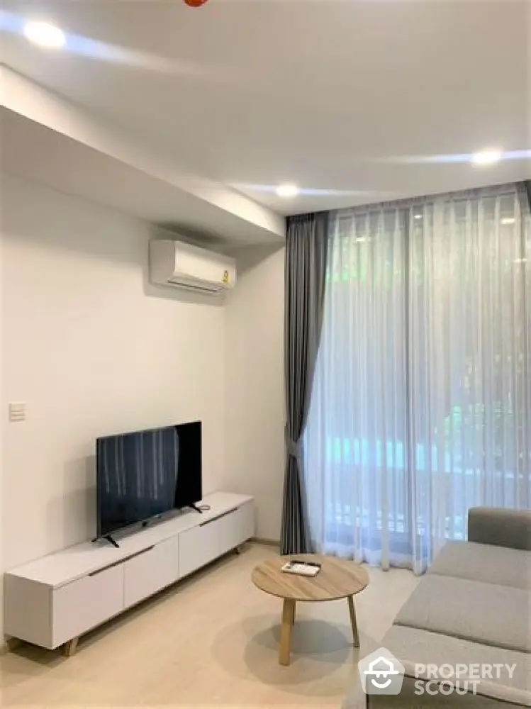 Modern living room with sleek furniture and ample natural light, featuring a wall-mounted TV, cozy sofa, and elegant sheer curtains.