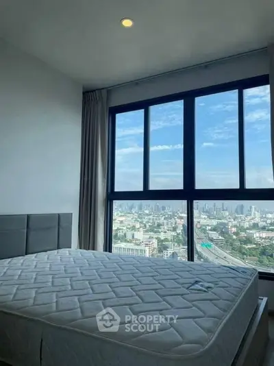 Spacious bedroom with stunning city view from large windows in modern high-rise apartment.