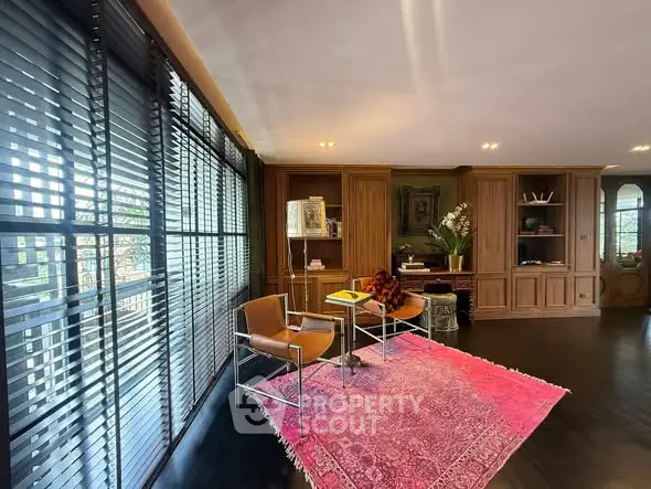Elegant living room with wooden cabinetry and large windows, featuring a vibrant pink rug.