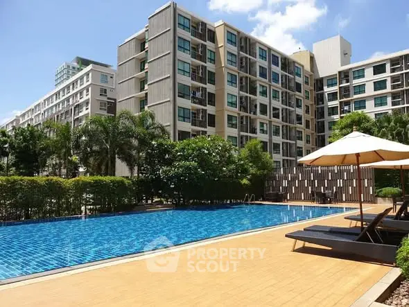 Modern condominium with luxurious pool and sun loungers under clear blue sky.