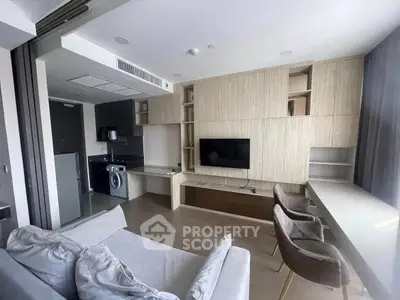 Modern living room with built-in storage, TV, and compact kitchen area featuring a washing machine.