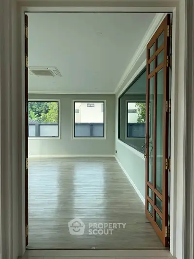 Spacious empty room with large windows and wooden flooring, perfect for customization.