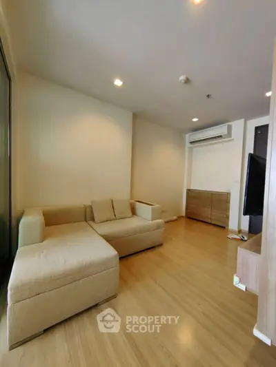 Spacious living room with modern beige sofa and wooden flooring, ideal for relaxation.