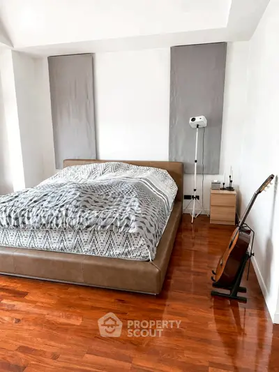 Modern bedroom with stylish decor and wooden flooring, featuring a cozy bed and guitar stand.