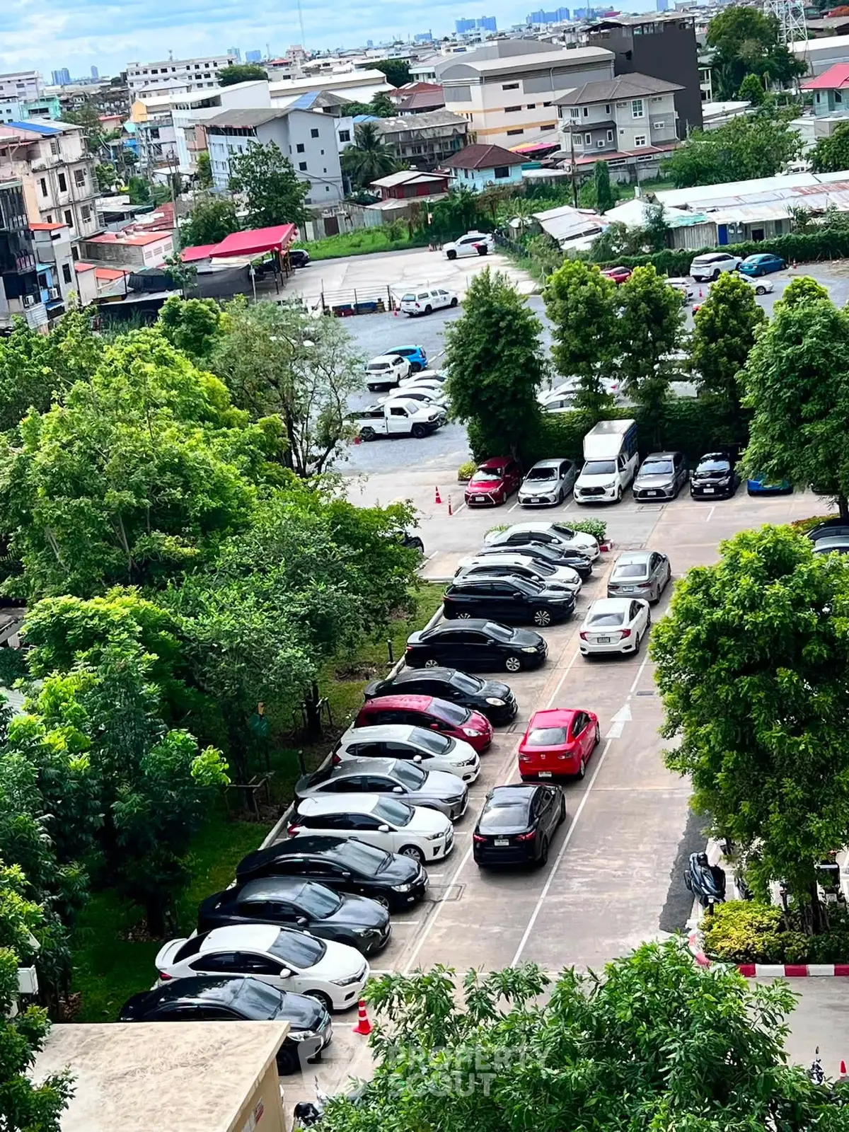Aerial view of a parking lot surrounded by lush greenery and urban buildings.