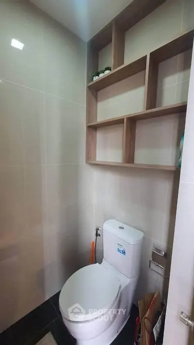 Modern bathroom with sleek toilet and wooden shelving, ideal for compact spaces.