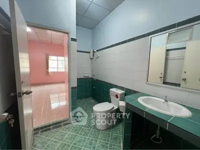 Spacious bathroom with green tile accents and modern fixtures, adjacent to a bright room with large window.