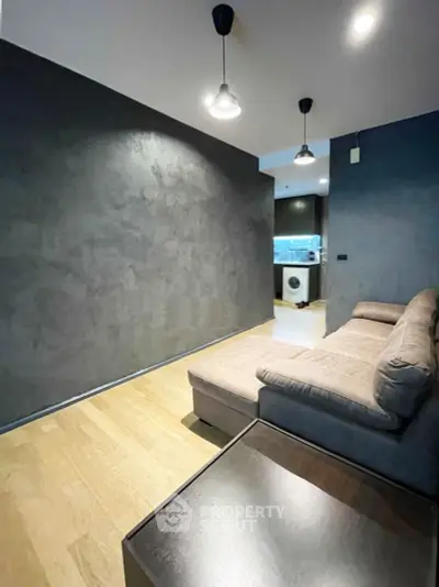 Modern living room with sleek design and cozy sofa, featuring a view into a stylish kitchen with washing machine.