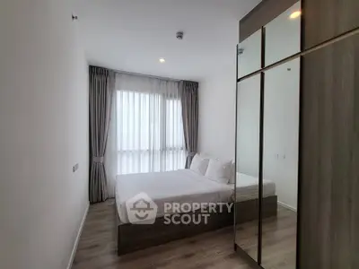 Modern bedroom with large window and mirrored wardrobe in stylish apartment.