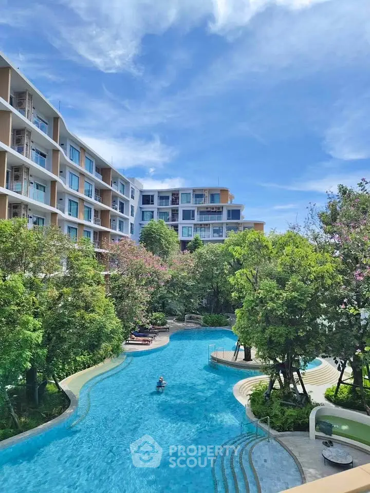 Luxurious residential complex with stunning pool and lush greenery under a clear blue sky.