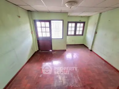 Spacious empty room with wooden flooring and natural light from windows.