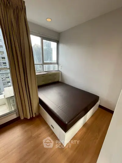 Cozy bedroom with city view, featuring a comfortable bed and large windows for natural light.