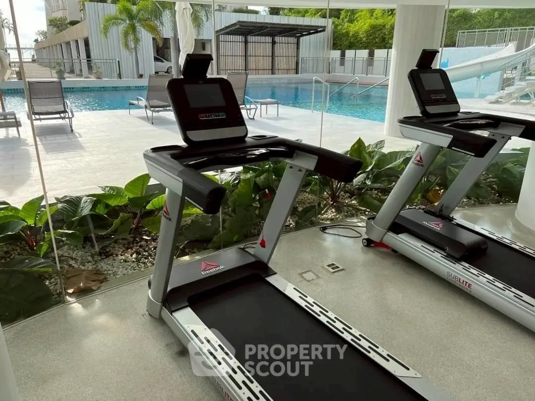 Modern gym with pool view, featuring state-of-the-art treadmills and lush greenery.
