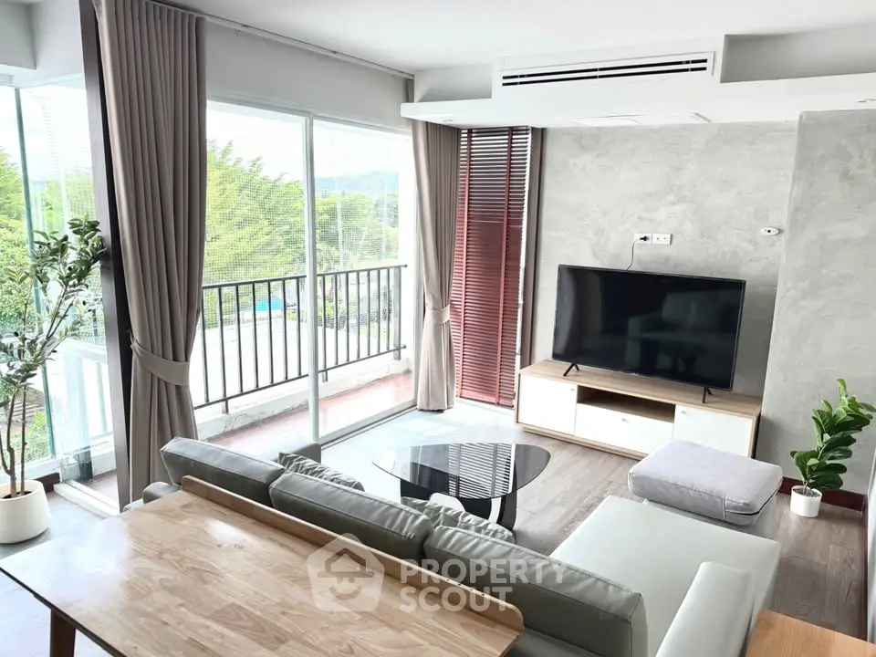 Modern living room with large windows and balcony view, featuring sleek furniture and stylish decor.