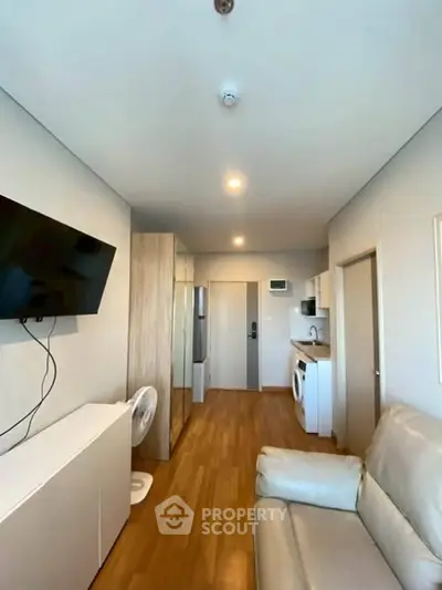 Modern living room with sleek furniture and appliances, featuring a wall-mounted TV and wooden flooring.