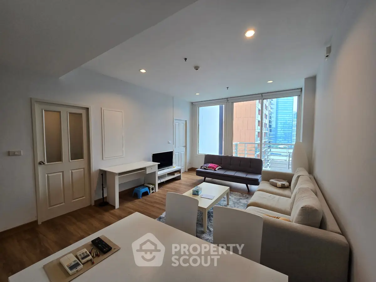Spacious modern living room with large windows and city view, featuring cozy seating and stylish decor.