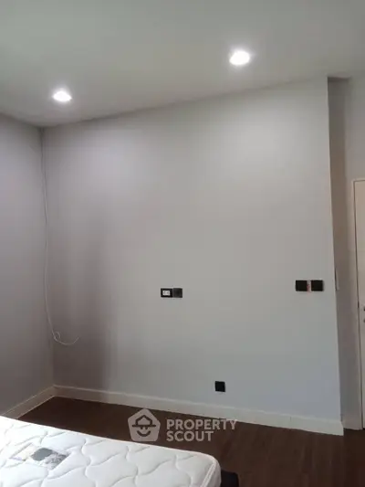 Minimalist bedroom with white walls and wooden flooring, featuring a mattress and modern lighting.