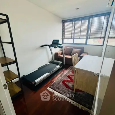 Cozy home office with treadmill, desk, and sofa in bright room with wooden floors.