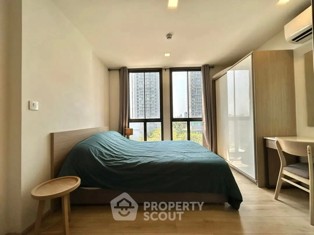 Modern bedroom with large windows and city view, featuring a cozy bed and stylish furniture.