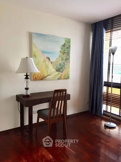 Charming study area with wooden desk, chair, and elegant lamp, featuring a large window with natural light.