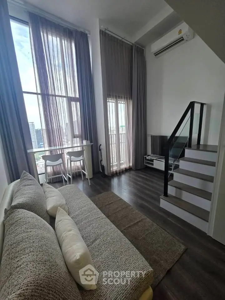 Modern living room with high ceilings, large windows, and a staircase, offering a bright and airy atmosphere.