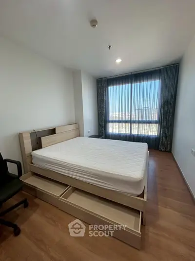 Spacious bedroom with large window and wooden flooring in modern apartment.